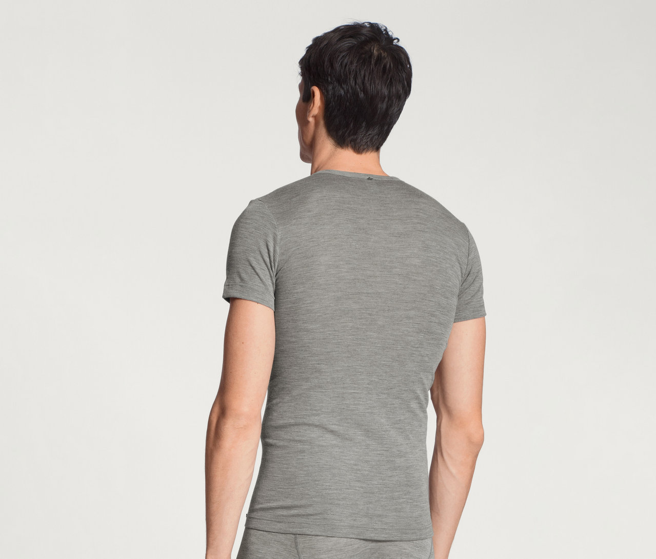 Mann von hinten in einem grauen Kurzarm-T-Shirt und passender Unterwäsche vor weißem Hintergrund.