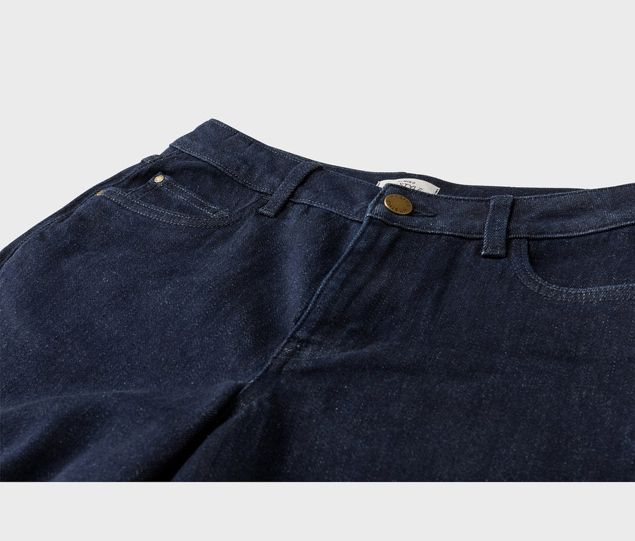 Nahaufnahme einer dunkelblauen Jeans, die den Bund, Gürtelschlaufen, Vordertaschen, eine kleine Münztasche mit Messingniete und einen Messingknopfverschluss zeigt.