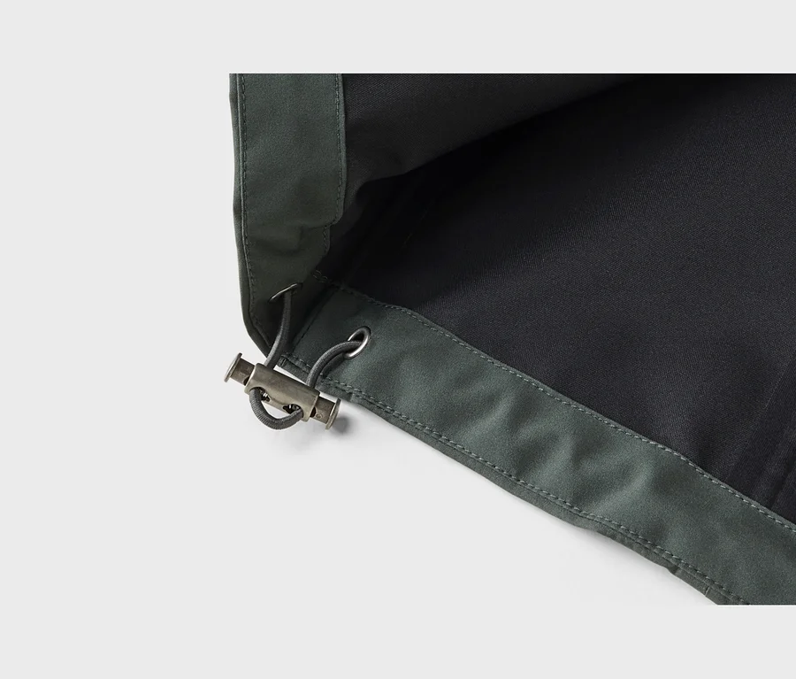 Nahaufnahme eines dunkelgrünen Stoffes mit Kordelzug und silberfarbenem Kordelstopper aus Metall. Der Stoffrand ist gesäumt mit sichtbaren Nähten, und ein dunkleres Futter ist innen sichtbar.