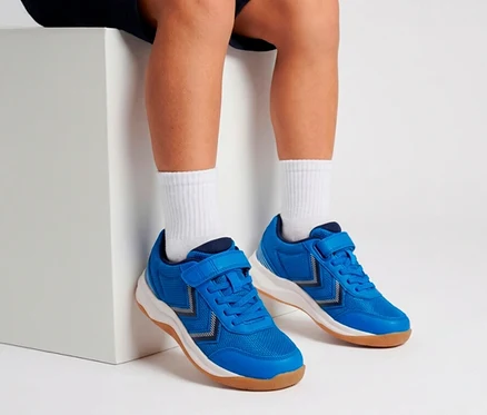 Beine und Füße einer Person mit blauen Turnschuhen mit Klettverschluss und weißen Socken, die auf einem weißen Block sitzt.