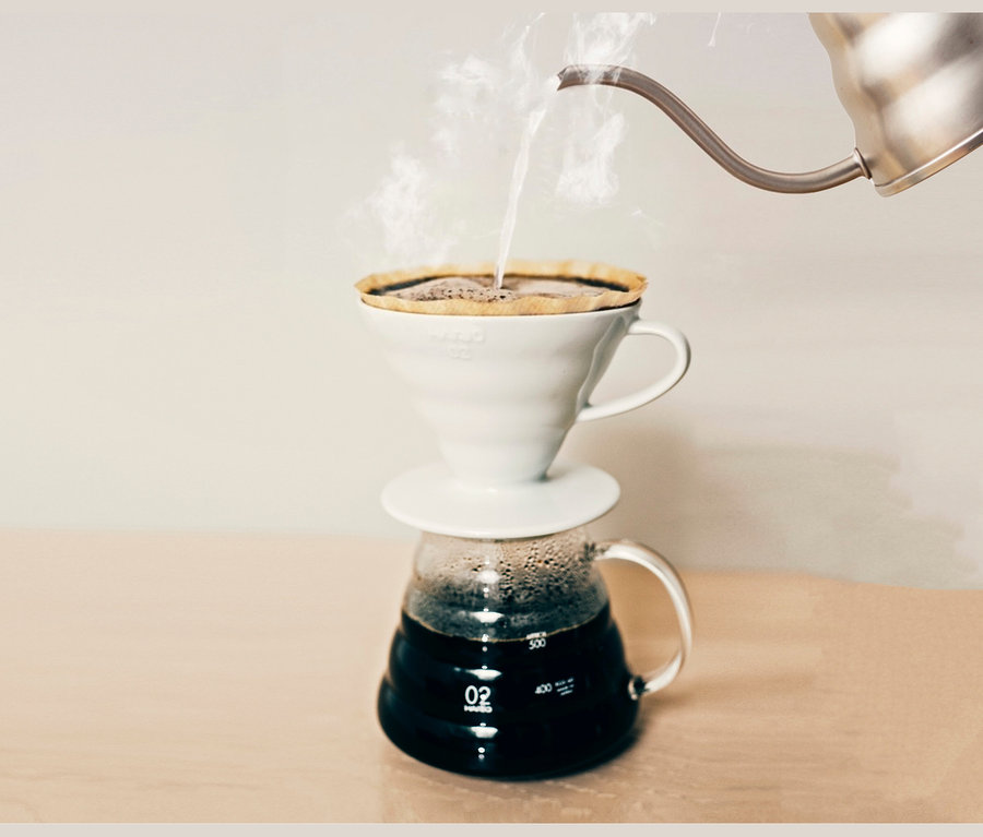 Heißes Wasser wird in einen HARIO V60 Keramikfilter gegossen, der auf einer Glaskaraffe steht.