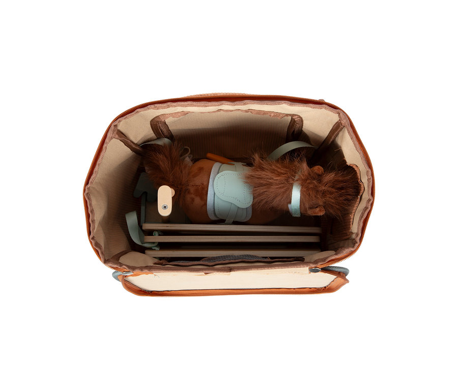 Ein dunkelbraunes Plüschpferd mit hellblauem Sattel und Zaumzeug ist in einem offenen, weichen, braunen Stall des small foot Spielsets verpackt. Flache Holzteile des Stalls sind unter dem Pferd sichtbar.