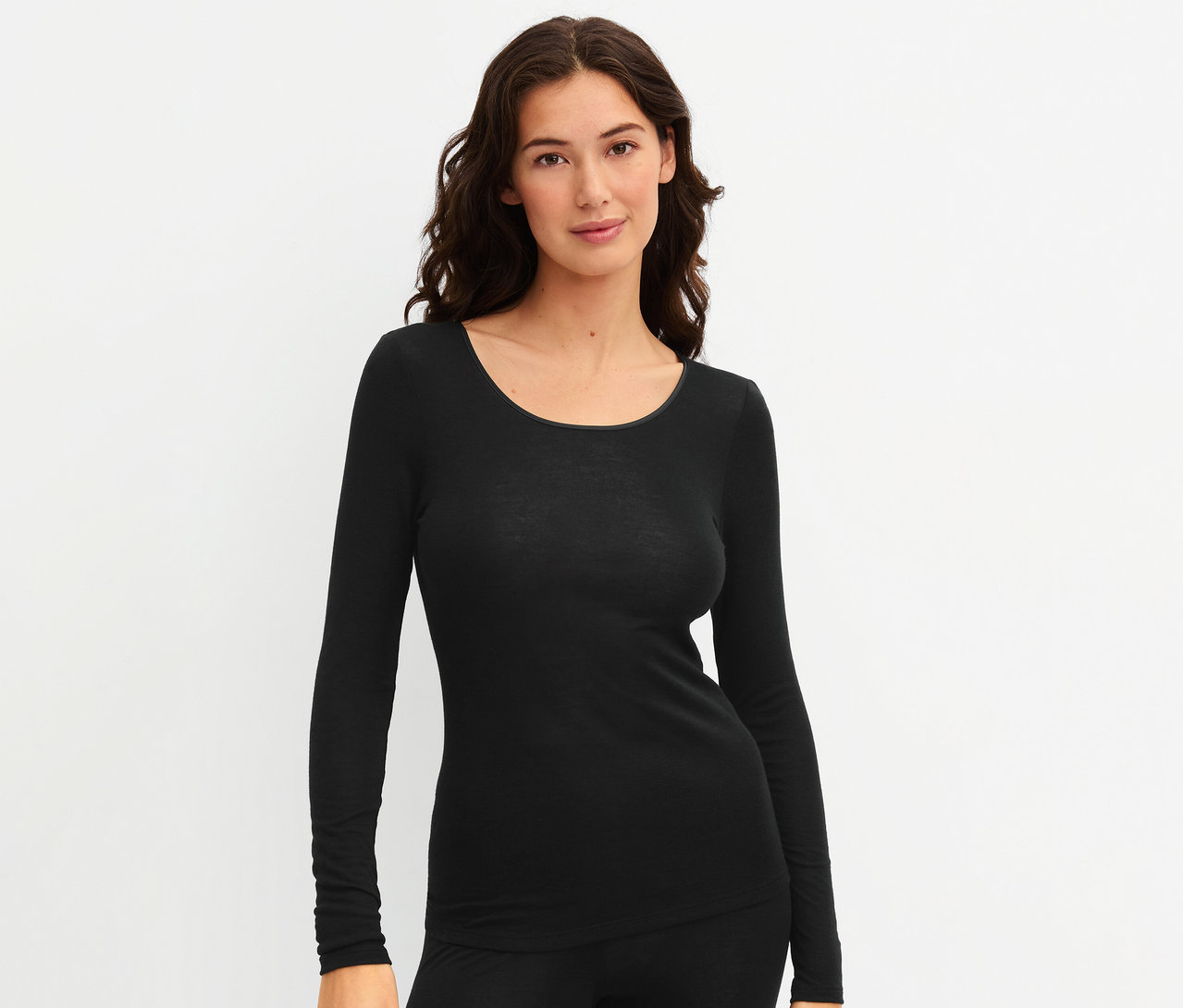 Frau trägt ein schwarzes CALIDA »True Confidence« Langarm-Shirt und eine schwarze Hose, blickt in die Kamera und lächelt.