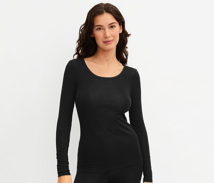 Frau trägt ein schwarzes CALIDA »True Confidence« Langarm-Shirt und eine schwarze Hose, blickt in die Kamera und lächelt.