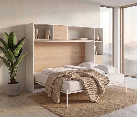 Ein weiß-holzfarbenes Roba Wandklappbett »Verso«, 120 x 200, ist in einem Raum mit großem Fenster und Bergblick ausgeklappt. Das Bett hat weiße Bettwäsche und eine beige Strickdecke. Darüber sind Regale mit Büchern und einer Vase. Links steht eine große Grünpflanze in einem grauen Topf auf einem Naturfaserteppich auf Holzboden.