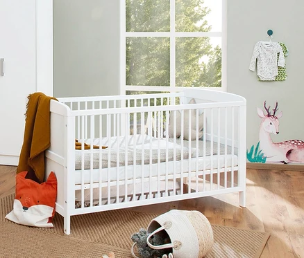 Ein Zimmer mit einem weißen Pinolino Babybett »Viktoria«, neben dem ein weißer Schrank steht und an der Wand eine Hirschdekoration angebracht ist.