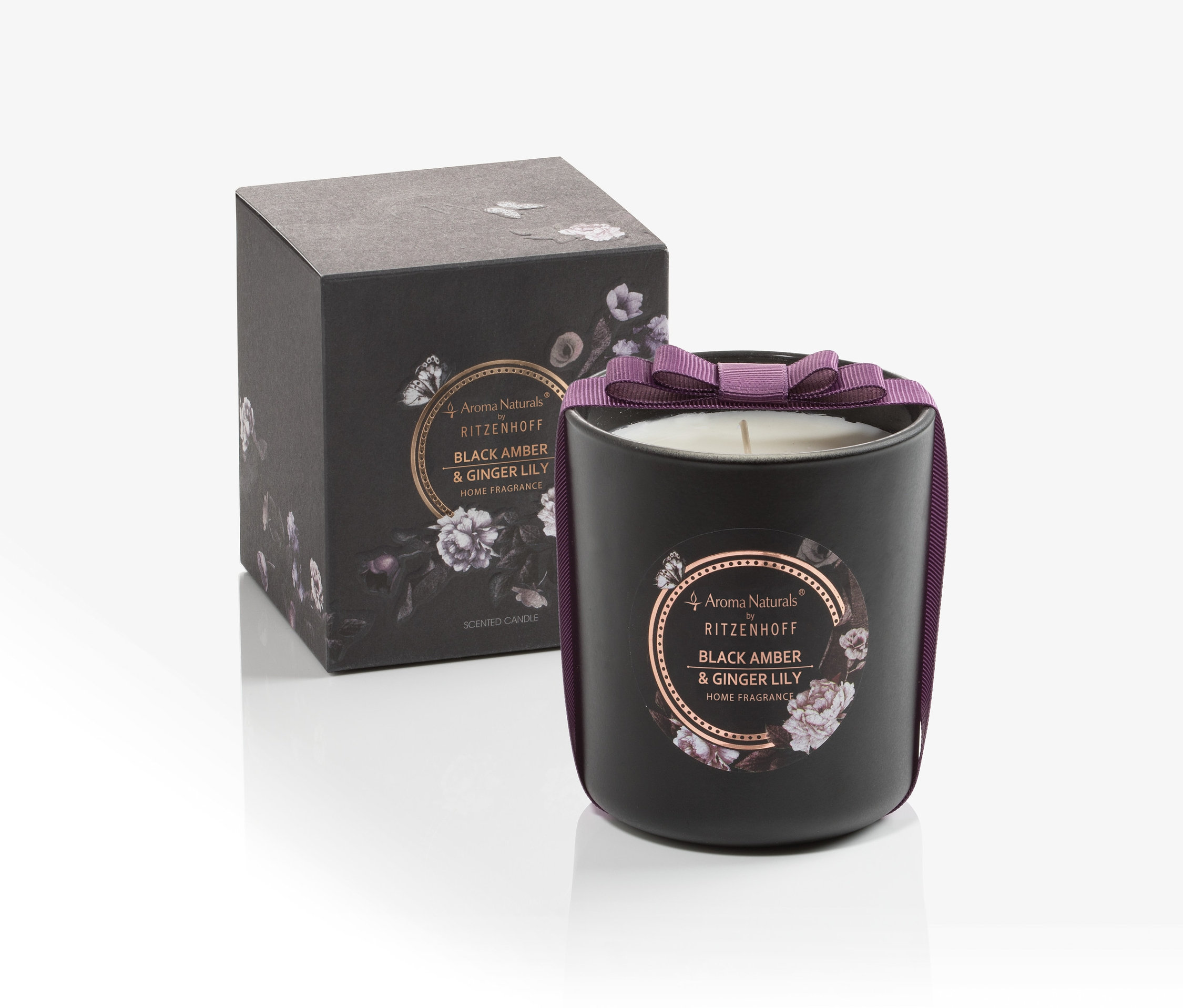Schwarze Duftkerze mit lila Schleife neben Schachtel.