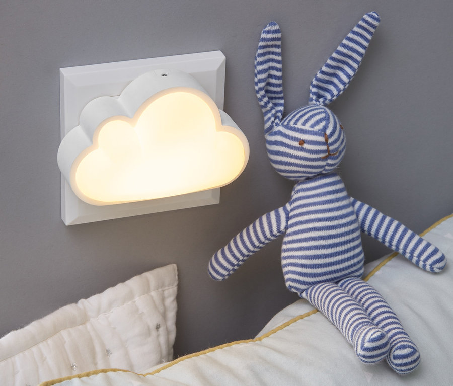 An der Wand montiert ist ein LED-Nachtlicht in Wolkenform . Auf dem Kissen sitzt ein Plüschhase.