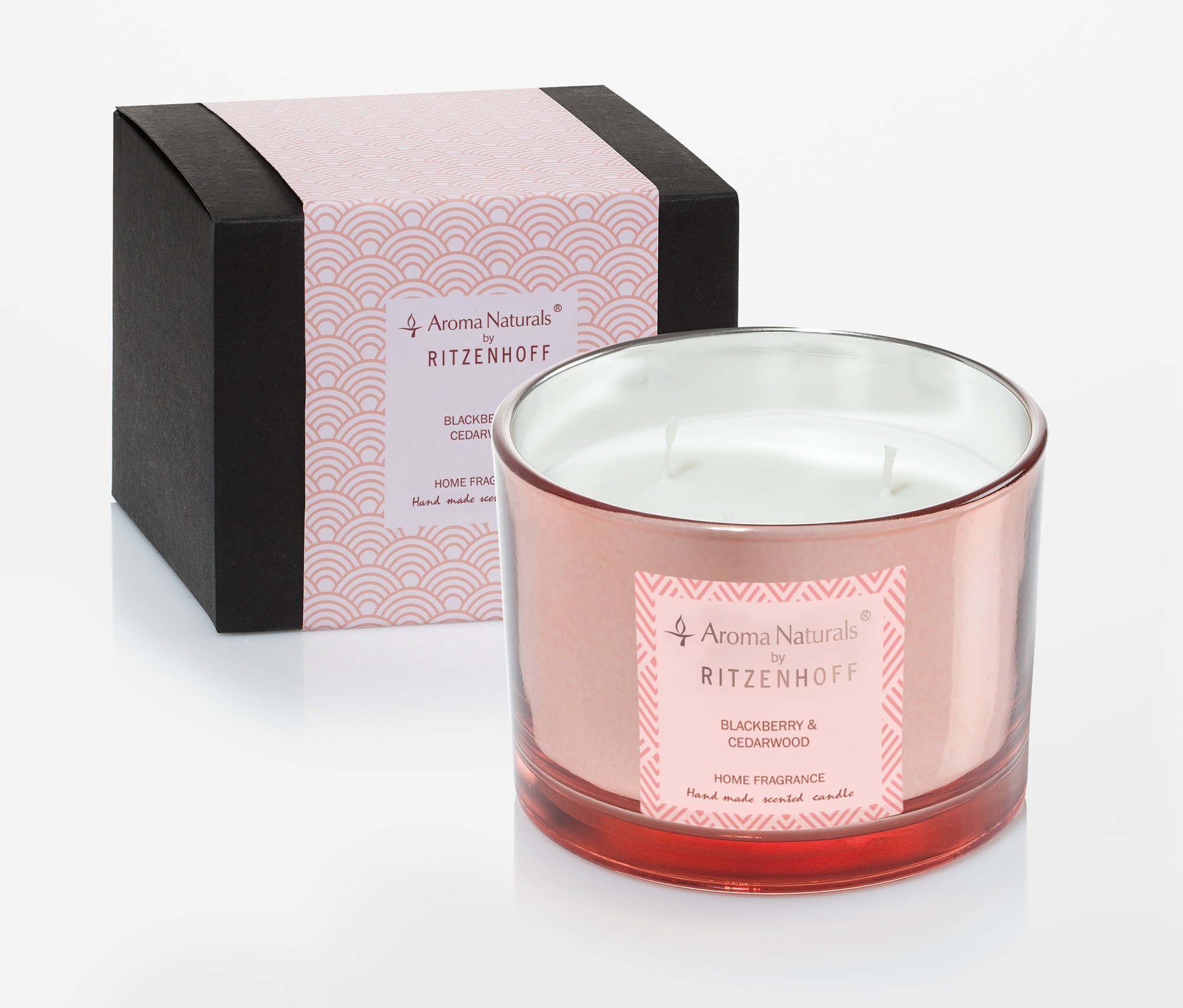 Dekorative Kerze im rosafarbenen Glas mit Etikett steht neben einer schwarzen Schachtel mit rosa Details.