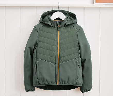 Eine grüne Hybridjacke hängt auf einem weißen Bügel vor einer weißen Wand.