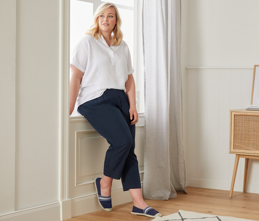 Frau sitzt auf einer Fensterbank, trägt eine Oversized-Bluse, eine lässige Chino und Espadrilles.