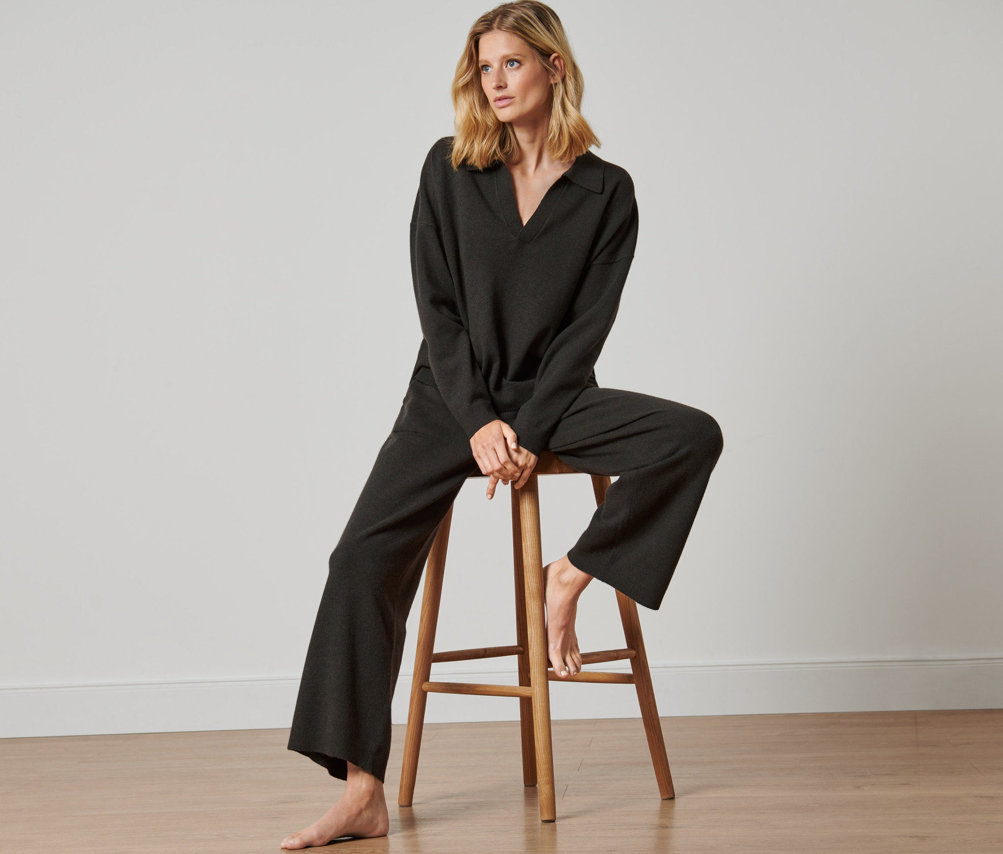 Frau sitzt auf einem Holzhocker und trägt eine Loungehose.