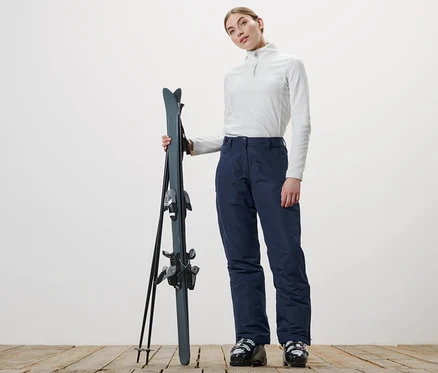 Frau hält Ski und trägt eine Skihose.