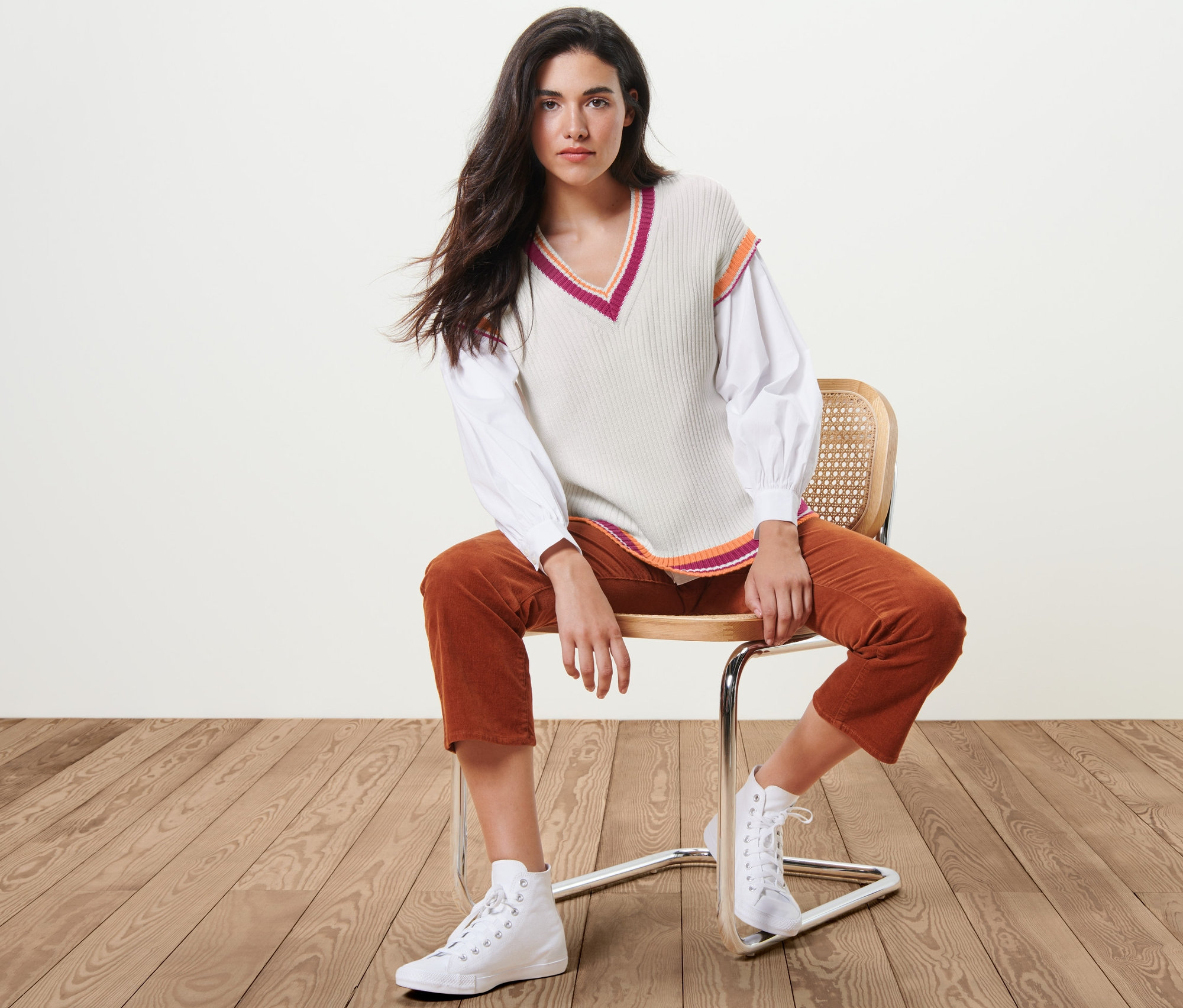 Frau sitzt auf einem Stuhl und trägt einen Strick-Pullunder.