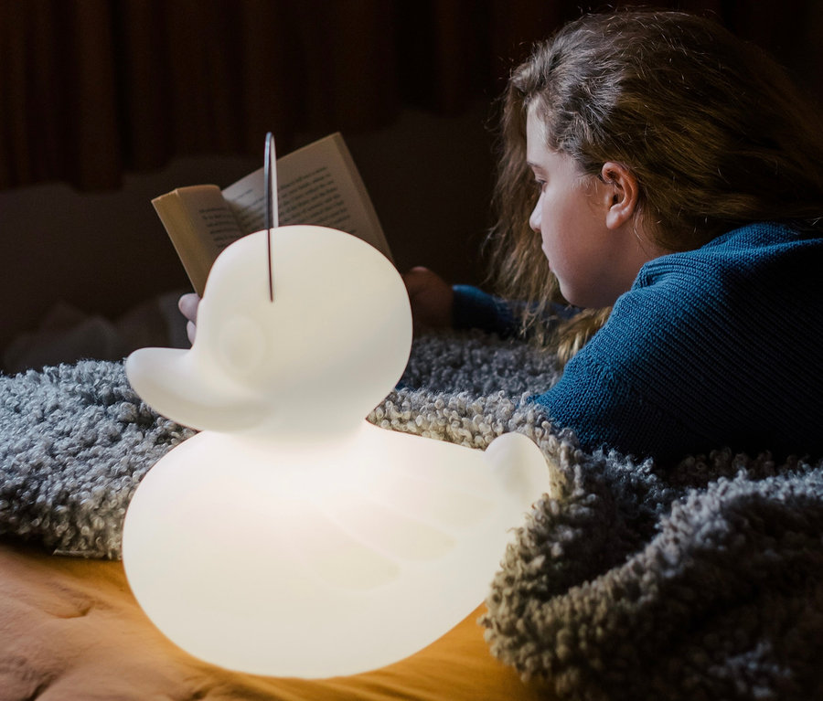 Mädchen liest Buch im Bett neben Goodnight Light LED-Leuchte »Ente« S.