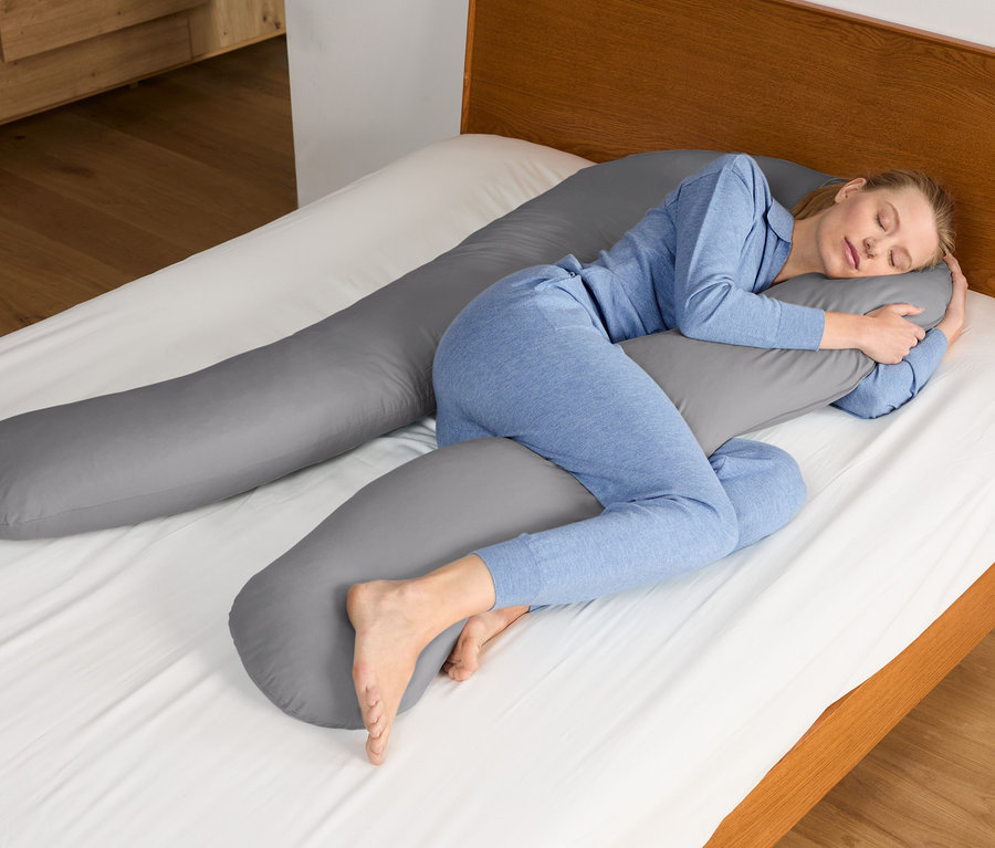 Eine Frau schläft mit einem Multifunktionskissen XXL im Bett.
