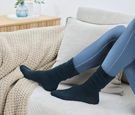Beine in blauen Leggings und 1 Paar Scrunch-Socken auf einem beigen Sofa.