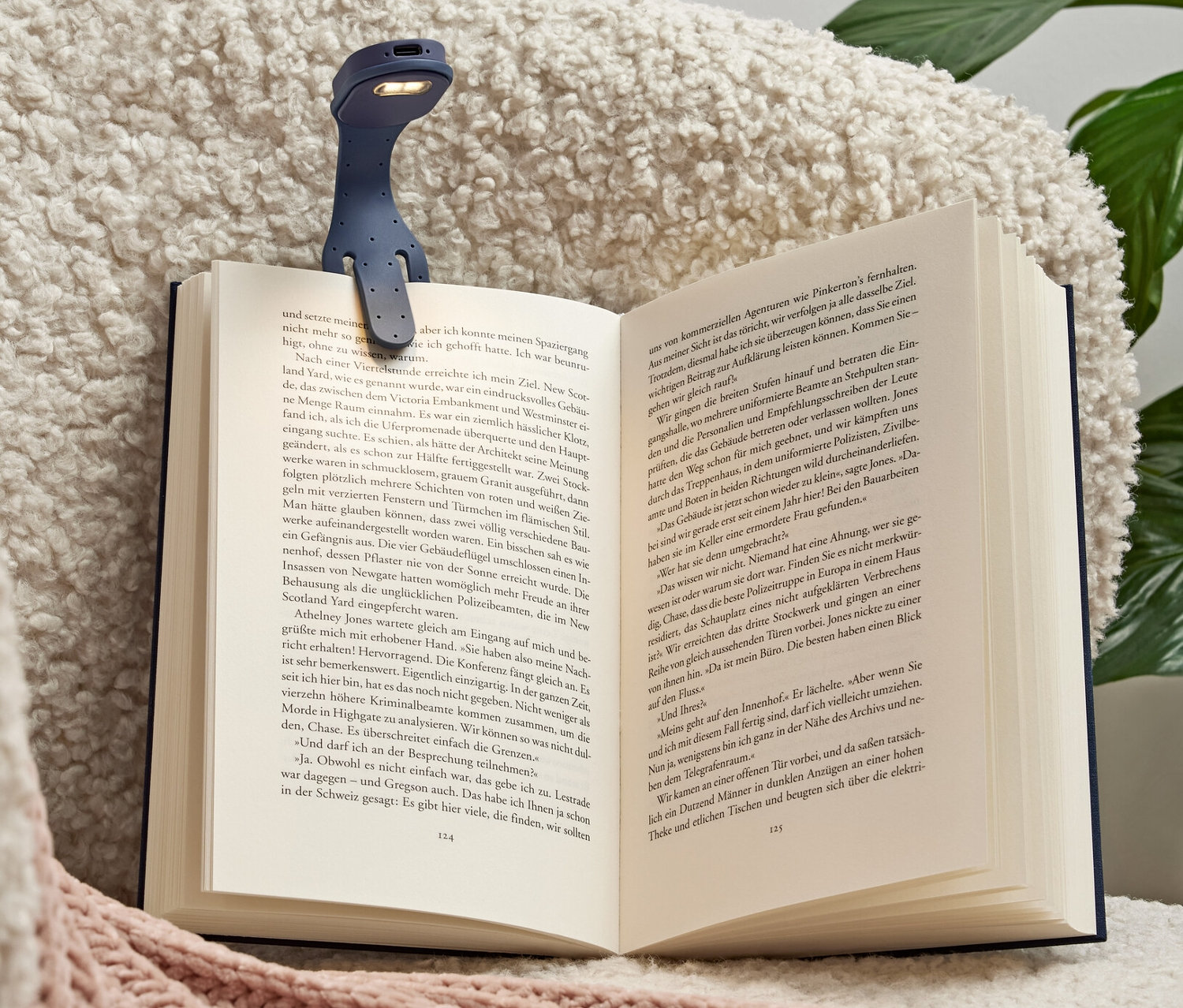 Eine blaue LED-Mini-Leselampe mit Akku ist an einem offenen Buch befestigt, das auf einem Sessel liegt.