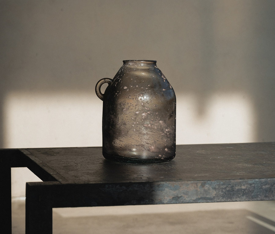 Eine graue Vase mit Henkel steht auf einem dunklen Metalltisch.