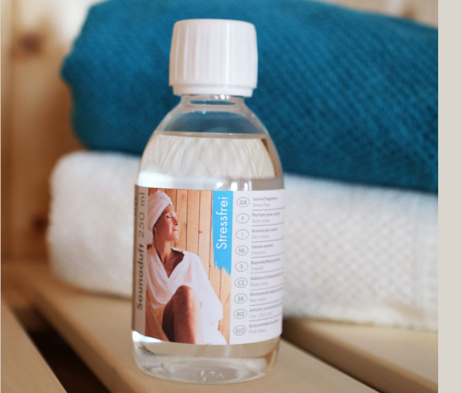 Eine Flasche Karibu Saunaduft steht auf einer Holzbank, dahinter liegen Handtücher.