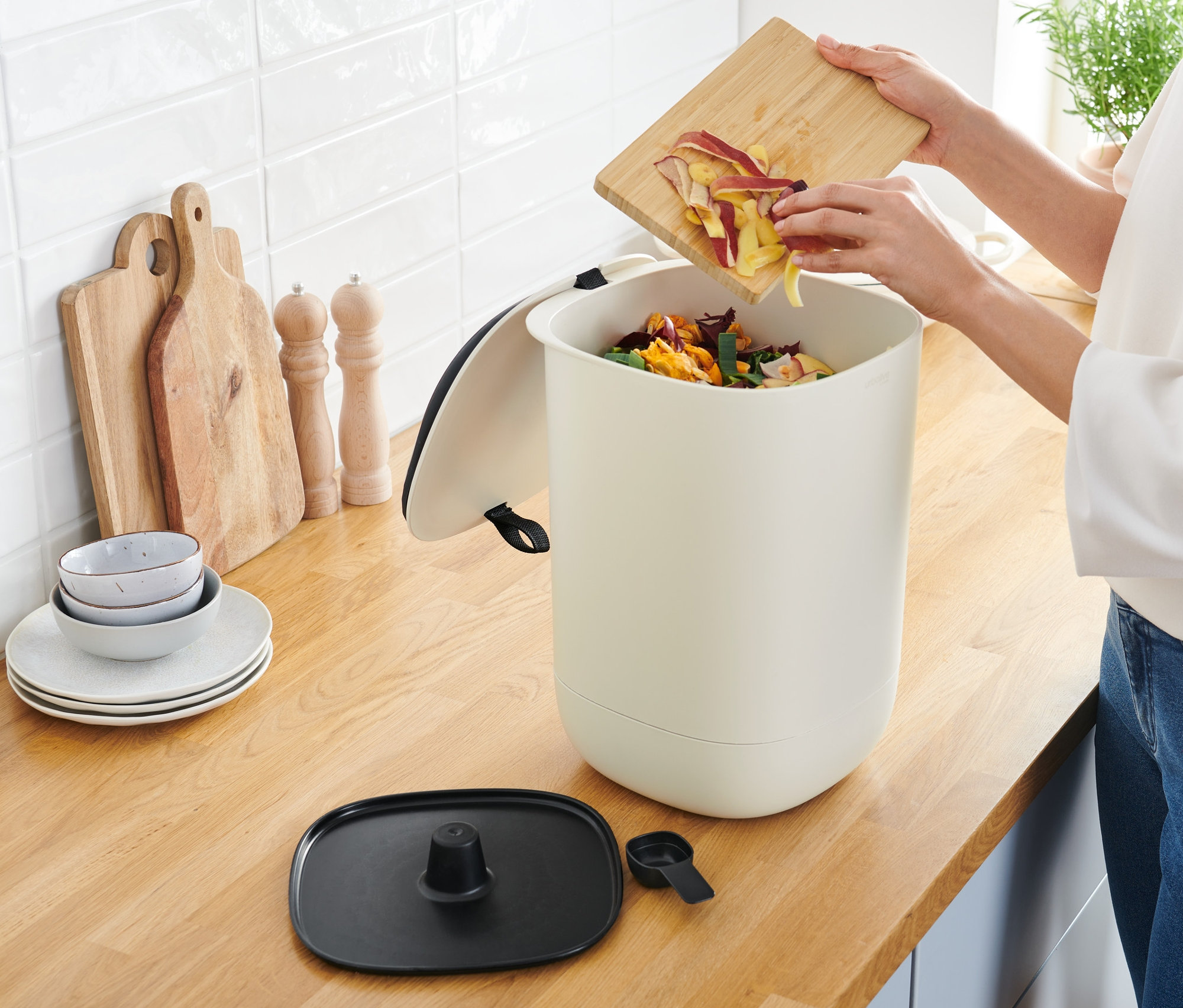 Frau leert Apfelschalen in einen Bokashi-Kompostier-Mülleimer.