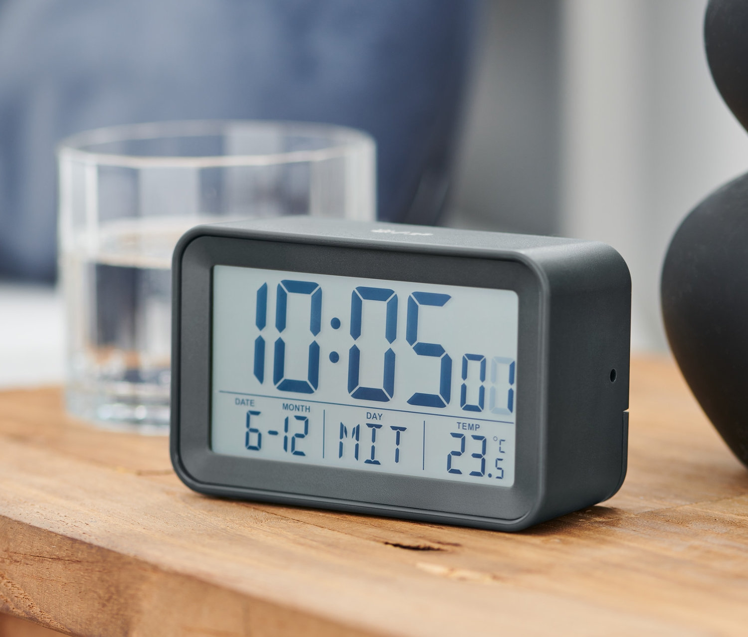 Grauer LCD-Funkwecker auf einem Holztisch zeigt die Zeit 10:05.