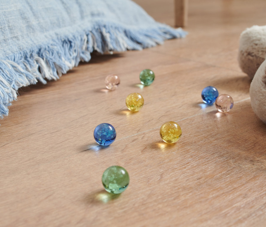 Leuchtmurmeln in verschiedenen Farben liegen auf dem Boden neben einem Plüschhund und einer blauen Decke.