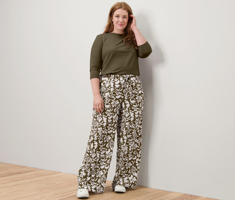 Eine Frau posiert in einem khakifarbenen Shirt mit 3/4-Arm und einer bedruckten Schlupfhose.