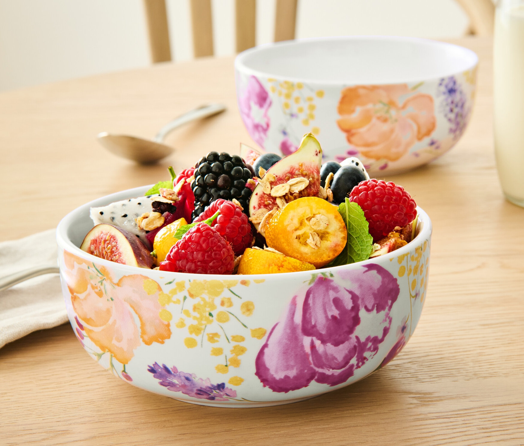 Auf einem Tisch stehen zwei mit Früchten gefüllte 2 Schalen, eine Milchflasche und eine Tasse mit Flüssigkeit.