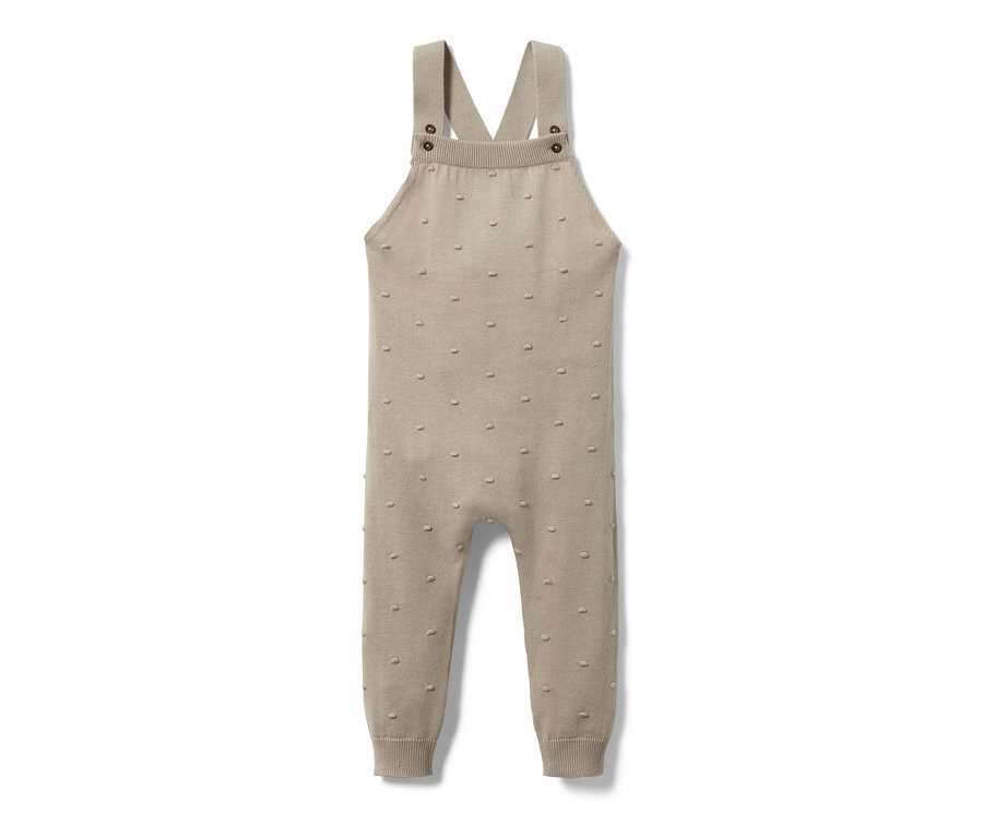 Eine beige Baby-Strick-Latzhose liegt auf einem weißen Hintergrund.
