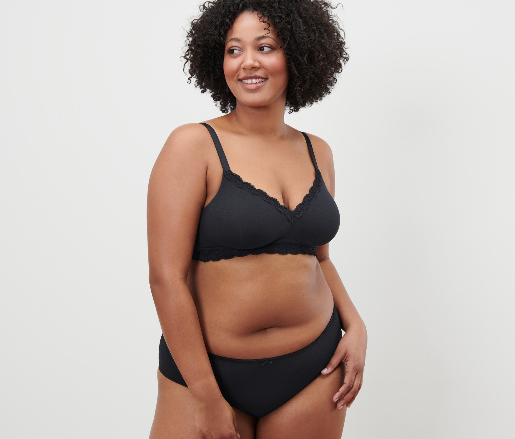 Frau mit lockigem Haar posiert in einem schwarzen Soft-BH.