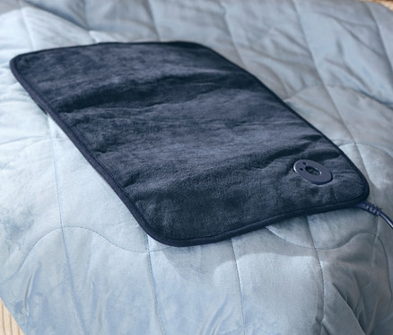 Beheizbare Schuhe und ein kleines Heizkissen liegen auf einer Entspannungs-Gewichtsdecke, 6 kg.