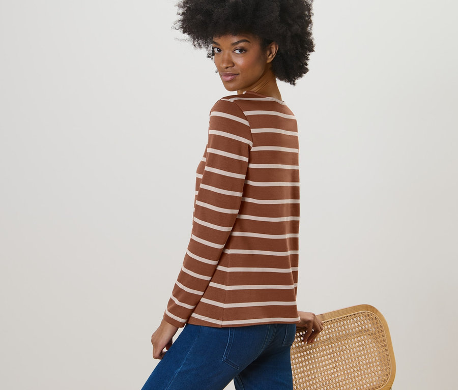 Frau posiert in einem gestreiften Langarmshirt in Cognac und blauen Jeans.