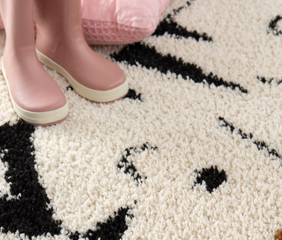 Rosa Gummistiefel und ein rosa Kissen liegen auf dem Kinderteppich NOMAD Tiger, Ø ca. 135 cm.