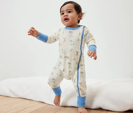 Kleinkind im Baby-Pyjama mit Tiermotiven steht auf einer Unterlage.