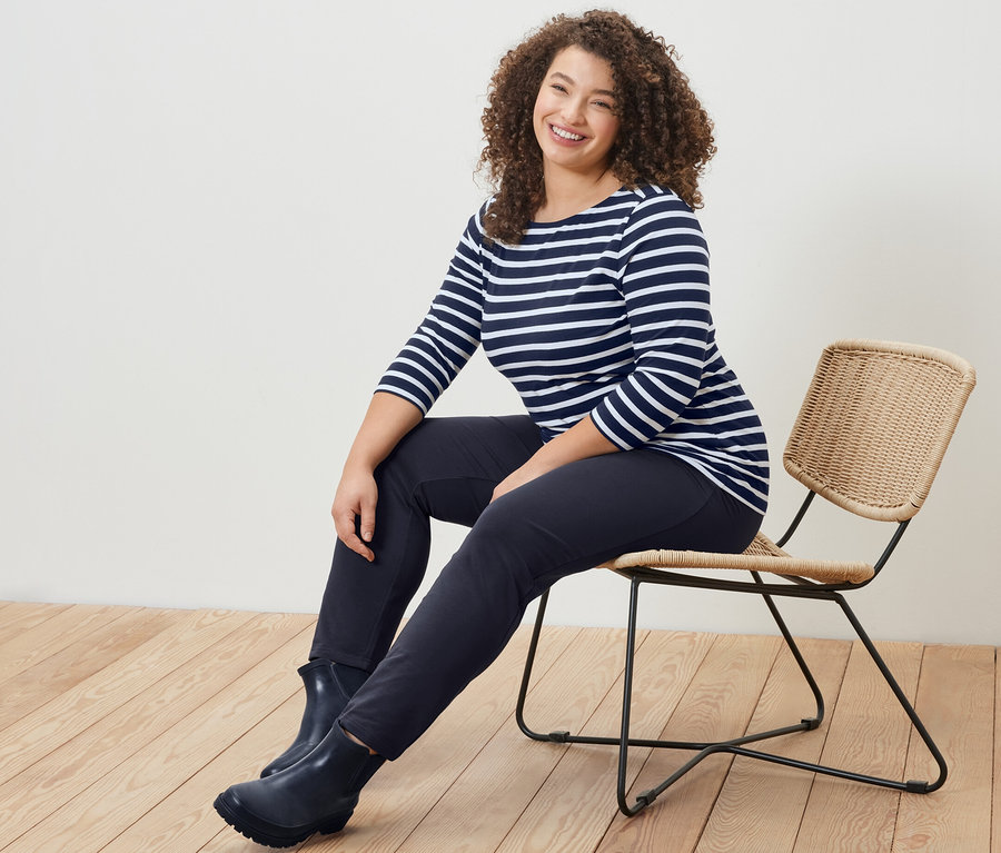 Eine Frau sitzt auf einem Stuhl und trägt ein gestreiftes Shirt mit 3/4-Arm und eine navy Joggpants.