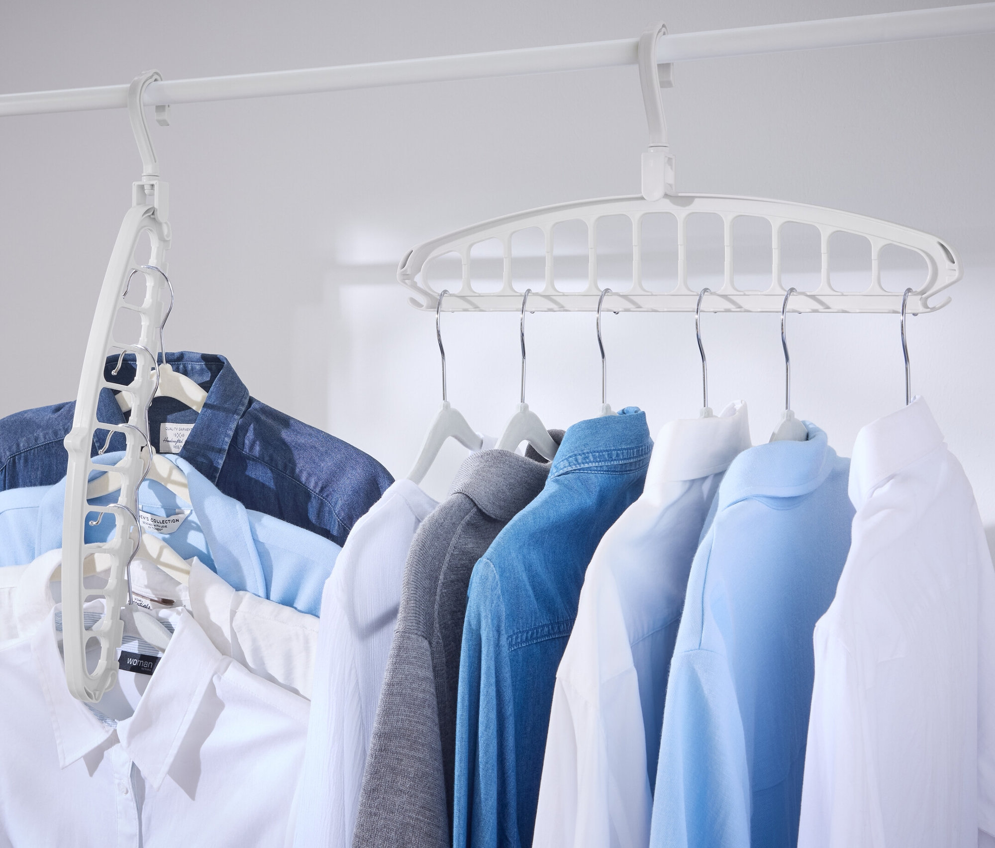 Mehrere Hemden hängen an einer weißen Stange mit einem 2 Multifunktions-Kleiderbügel.