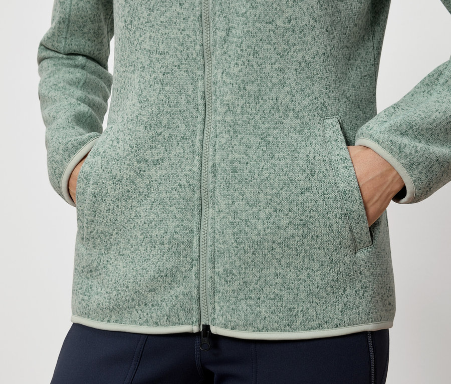 Person hat Hände in den Taschen einer grünen Fleecejacke.