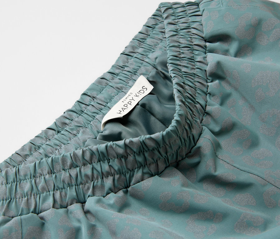 Nahaufnahme einer Kinder-Regenhose mit reflektierenden Elementen, elastischem Bund und Happy Kids-Etikett.