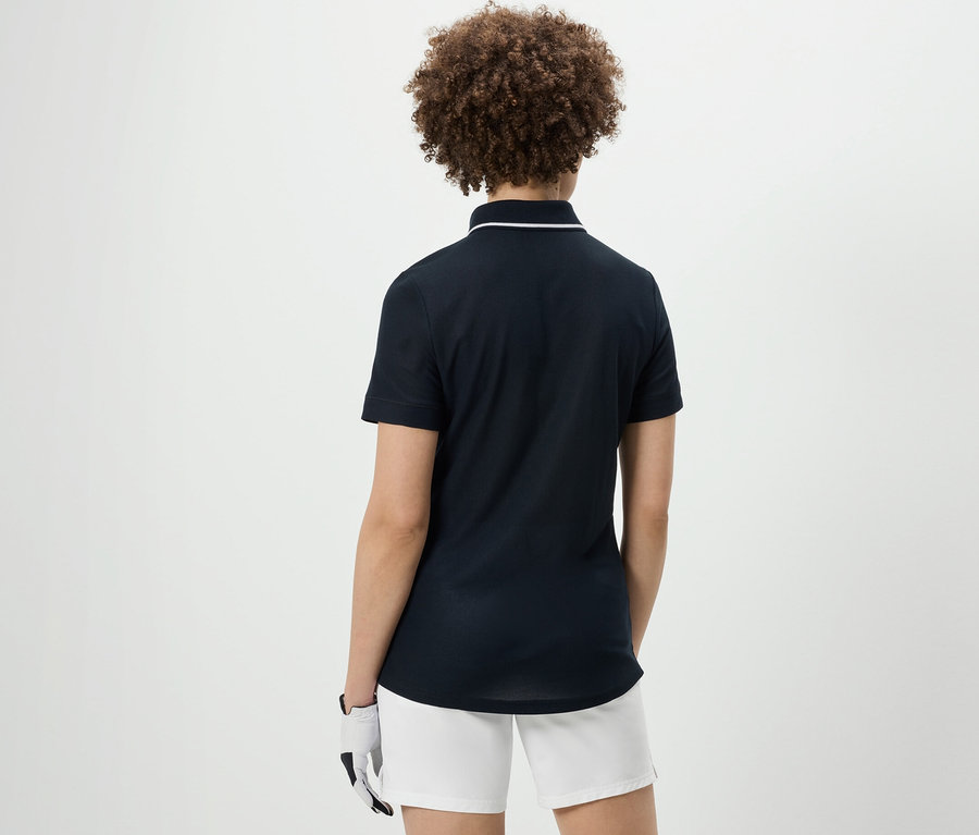 Rückansicht einer Frau mit lockigem Haar, die ein dunkelblaues Funktionspoloshirt und weiße Shorts trägt.