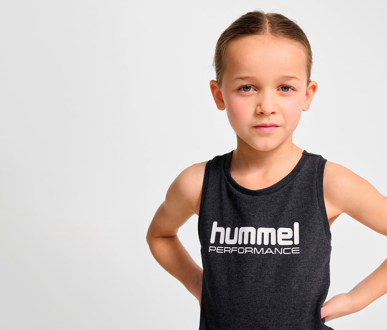 Porträt eines Mädchens mit den Händen in den Hüften, das ein schwarzes HUMMEL HMLJR Top trägt.