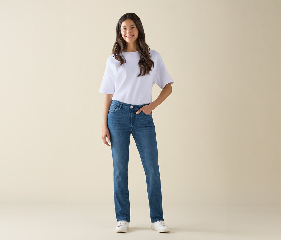 Eine Frau steht und posiert in blauen Jeans, einem weißen T-Shirt und weißen Schuhen.