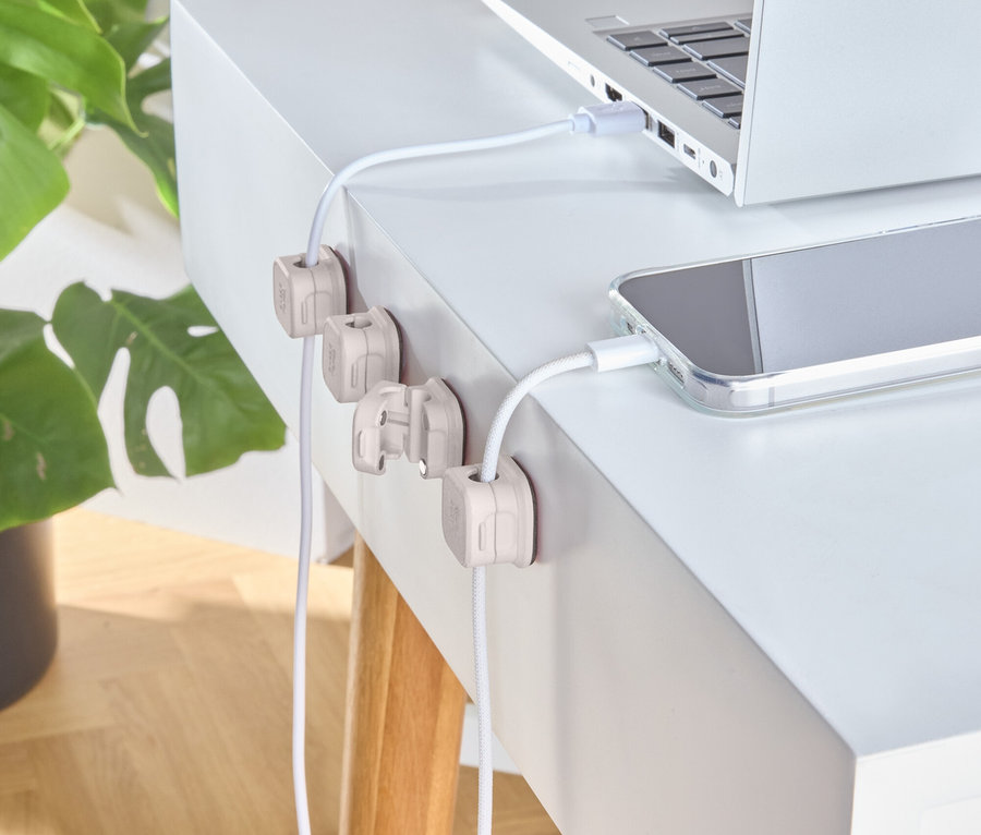 Silbernes Notebook und Telefon werden auf einem weißen Schreibtisch mit hölzernen Kabelhaltern aufgeladen.