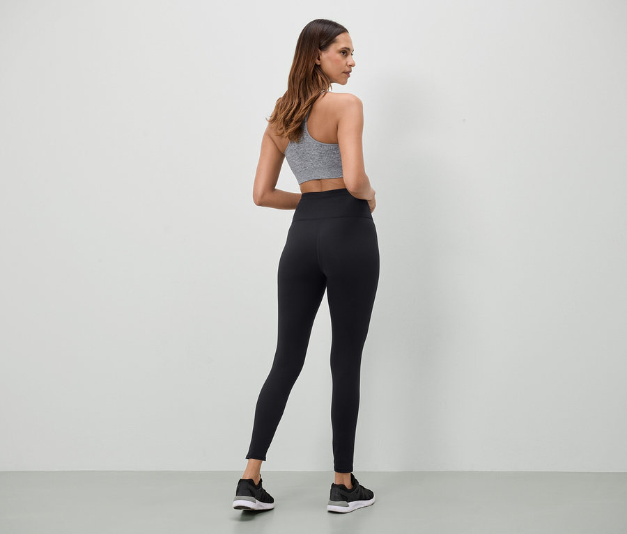 Frau in grauem Sport-BH und schwarzen Leggings steht mit dem Rücken zur Kamera.