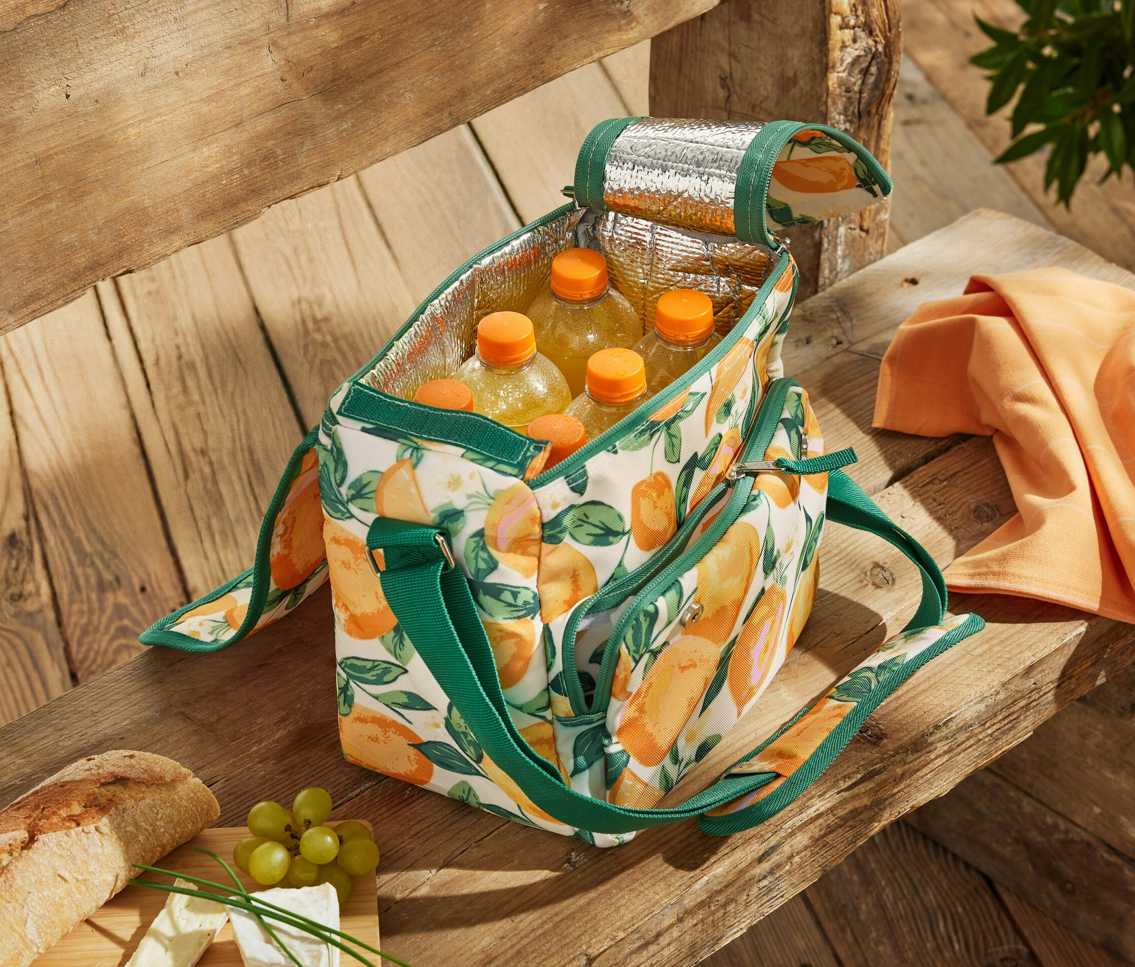 Eine offene Mini-Kühltasche mit Zitrusmuster gefüllt mit Flaschen auf einer Holzbank.