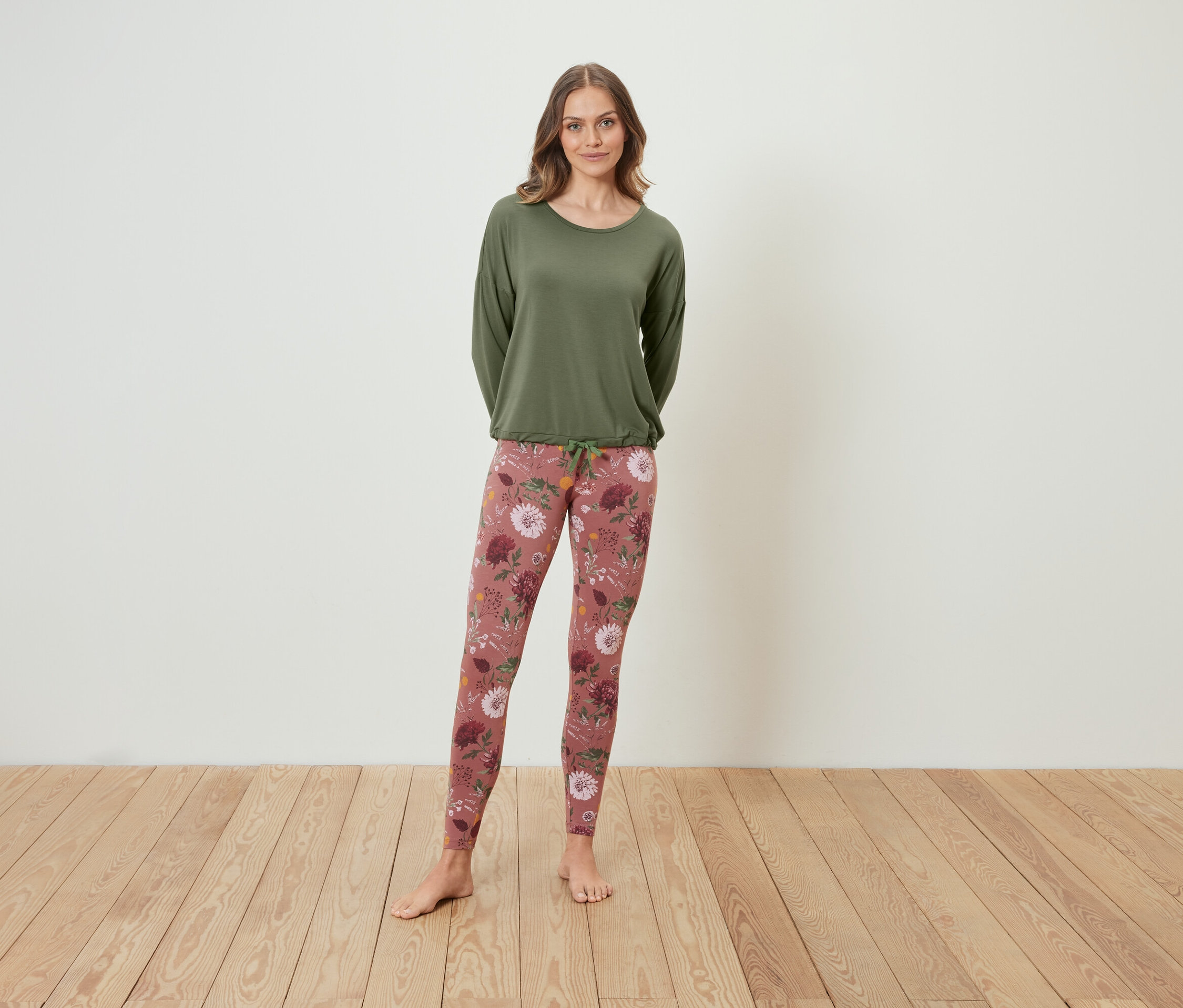 Frau steht und trägt ein grünes Langarmshirt und Leggings mit Blumenmuster.