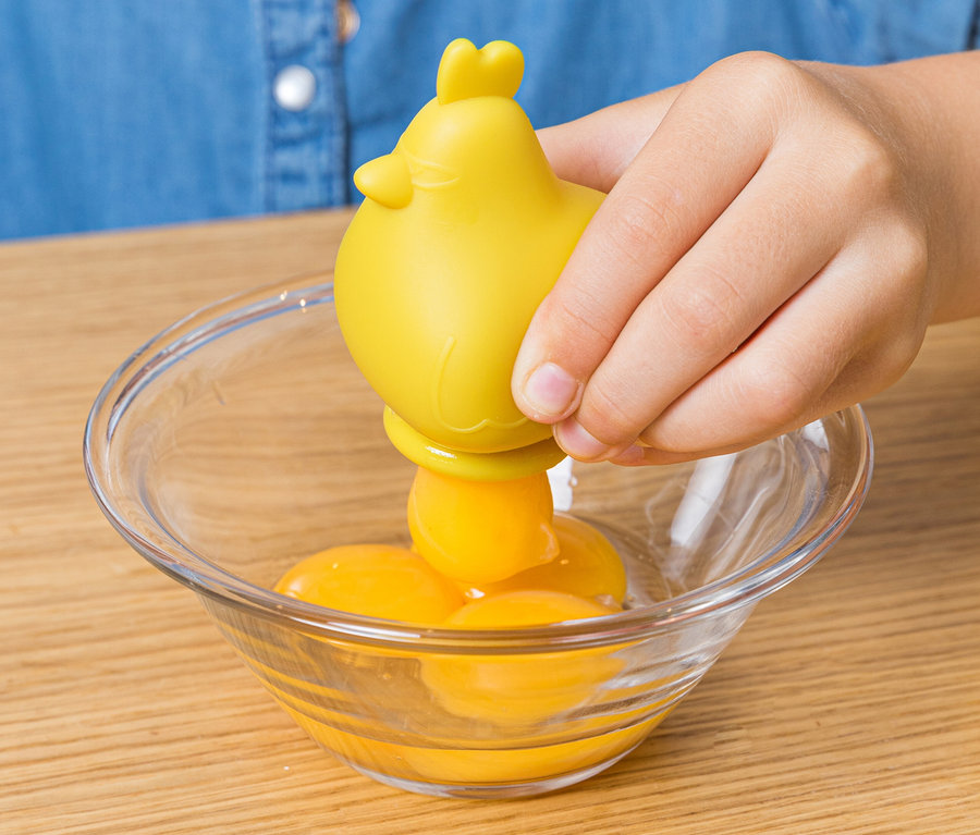 Ein Kind hält ein gelbes Küken über eine Glasschüssel mit Eigelb, möglicherweise aus dem Chefclub Dessert und Keks-Back-Set.