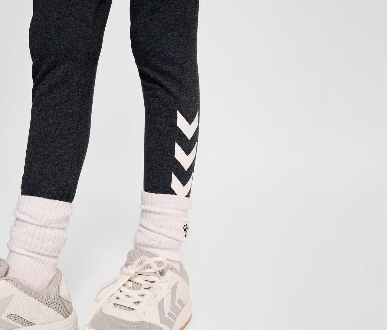 Beine einer Person in HUMMEL HMLJR Logo Tight, weißen Socken und Turnschuhen.