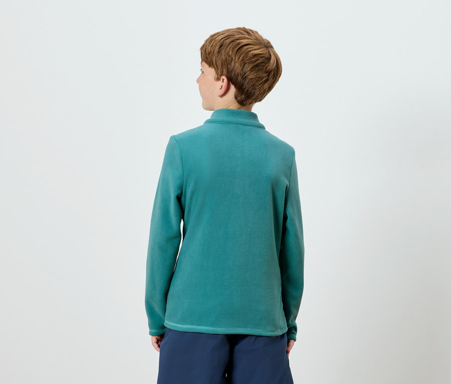 Von hinten ist eine Person mit kurzem braunem Haar zu sehen, die ein blaugrünes Langarm-Top und marineblaue Shorts trägt.