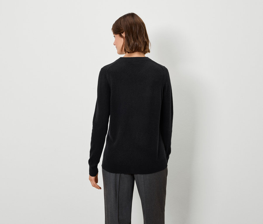 Frau mit braunen Haaren trägt einen schwarzen Pullover und graue Hosen, von hinten gesehen.